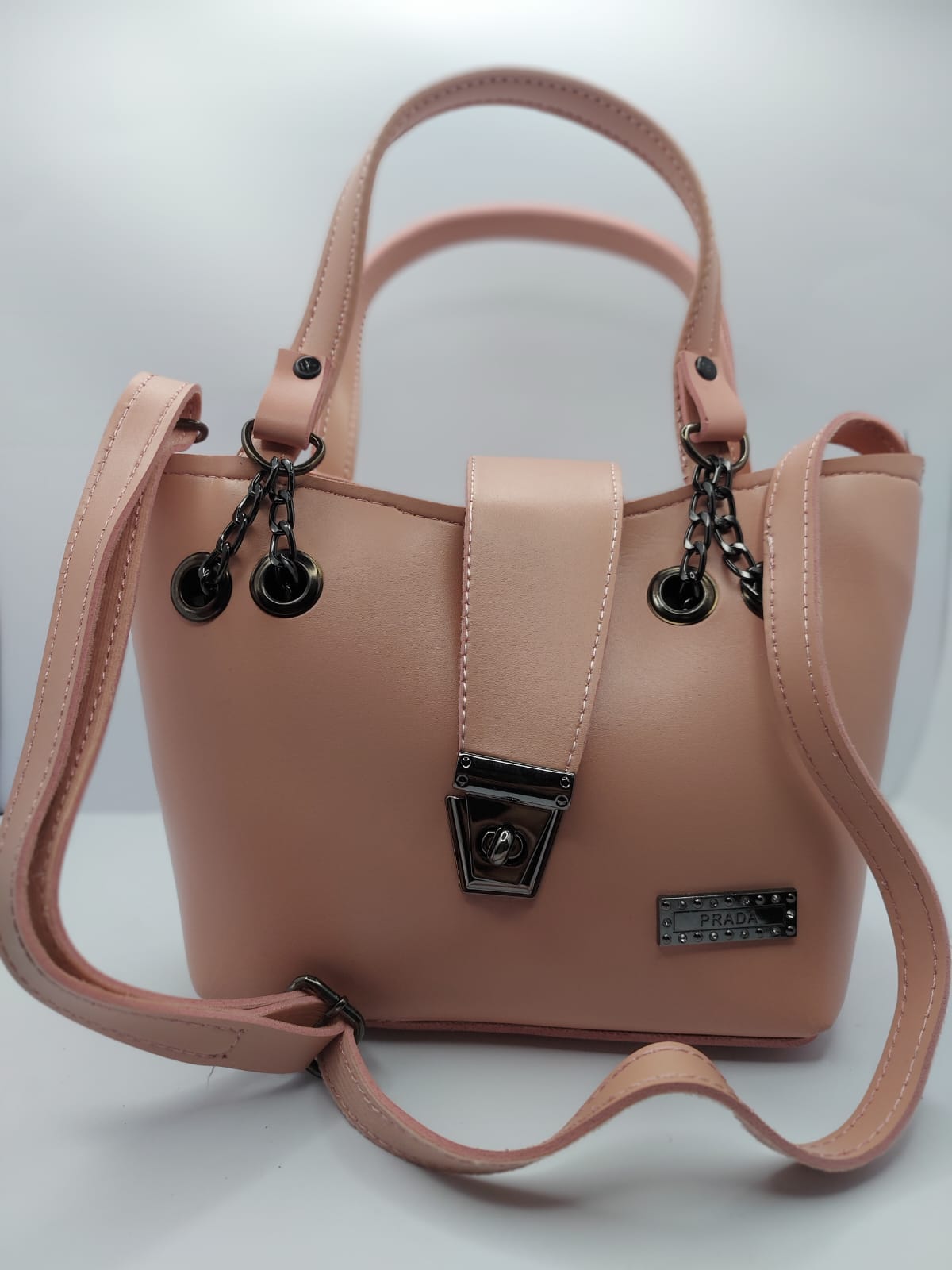 Radiant Peach tote bag with metallic twisted lock, made from premium PU leather. Features hand tote and adjustable shoulder straps, dual zippers for storage, and a sleek solid design with metallic details. Perfect for daily use or special occasions