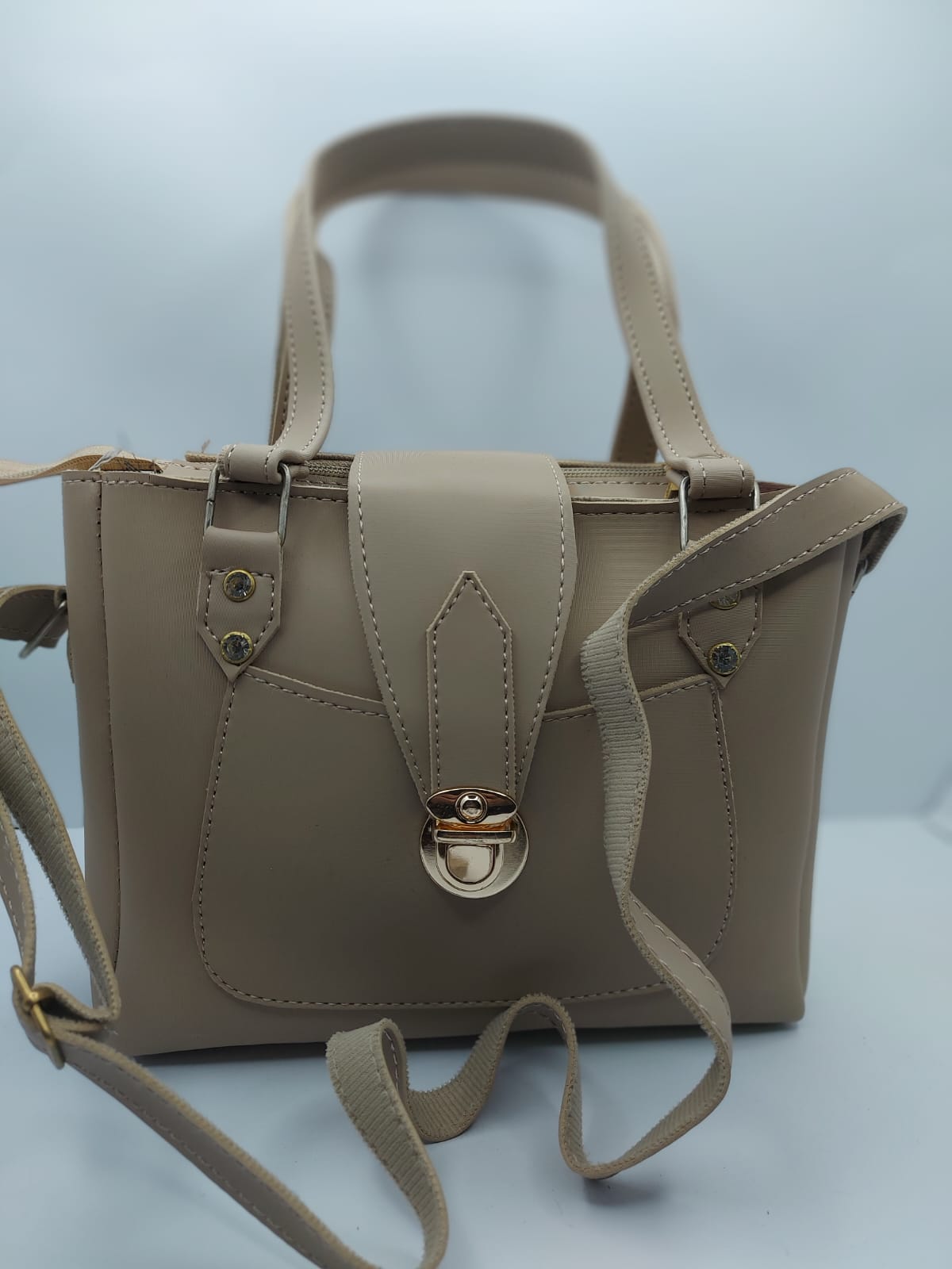 Warm Beige Regal Carry Tote Bag made of premium synthetic leather with neat stitching. Features a gold-tone lock closure, a front pocket for easy access, and an internal zippered compartment for organization. Offers dual carrying options: hand tote and adjustable shoulder strap