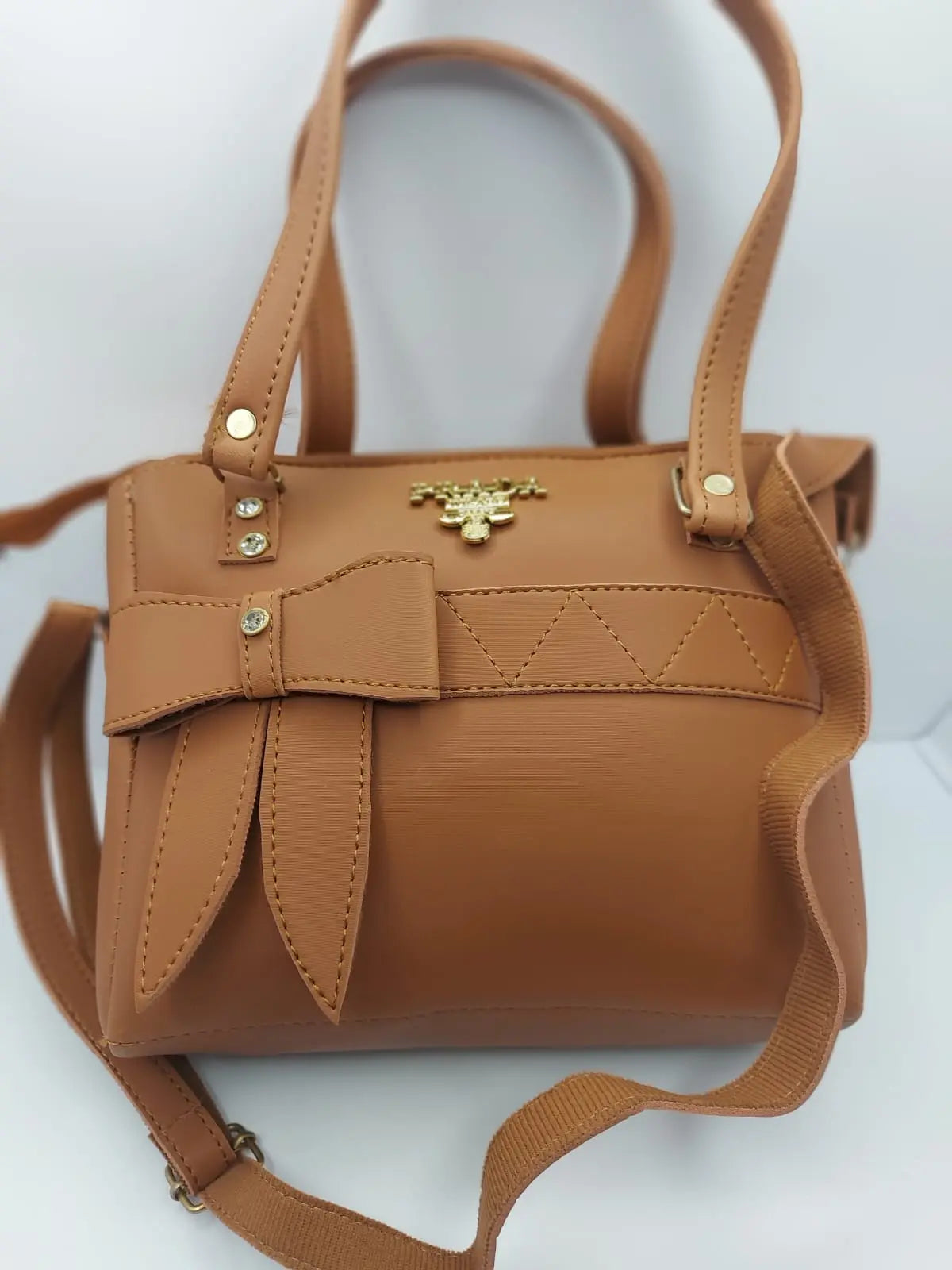 Luxurious camel brown tote bag with a silk-textured finish, bow charm accent, gold-tone Prada-inspired logo, and dual carrying options for versatile styling