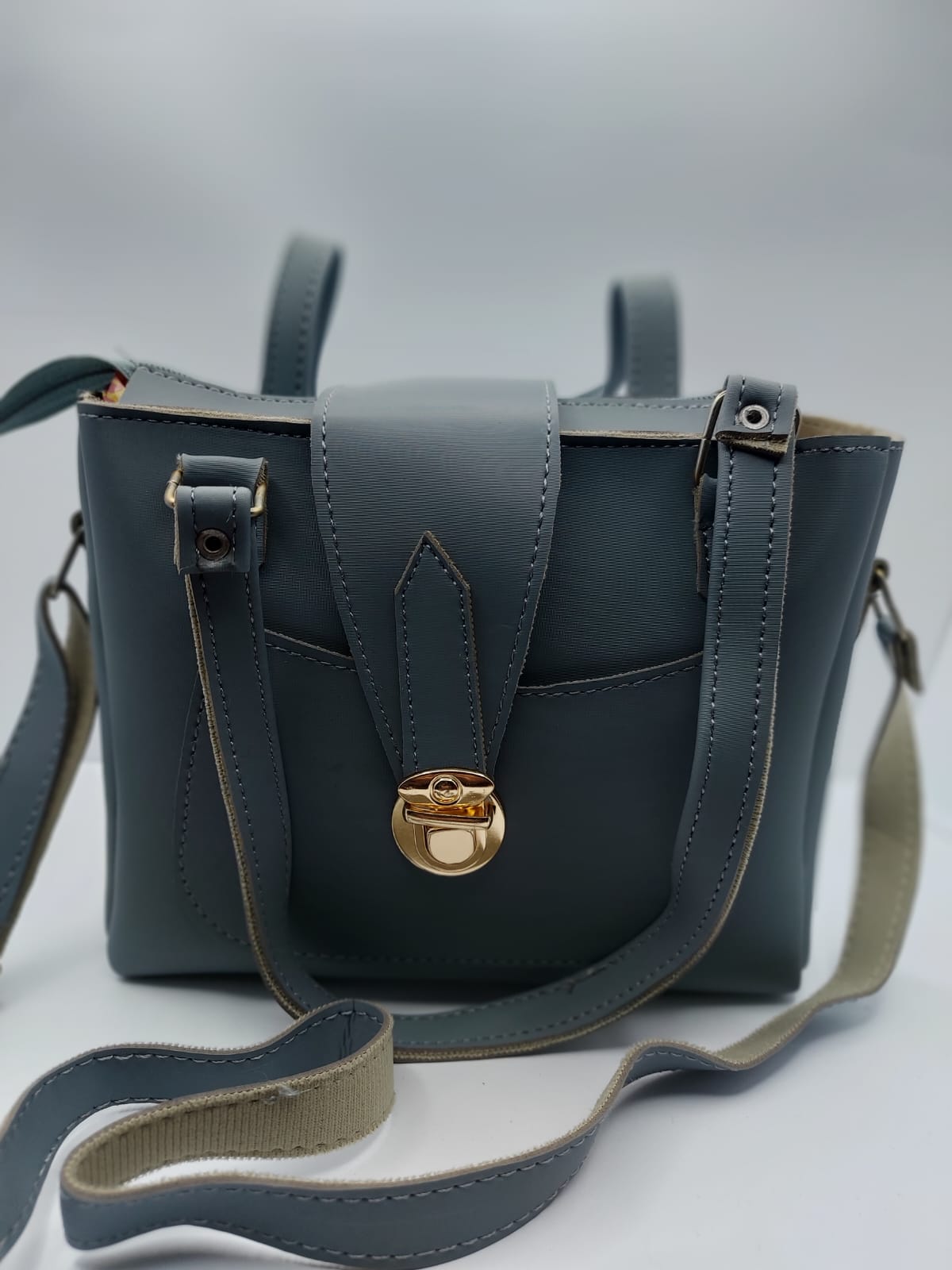 Stylish slate gray tote bag with a gold-tone lock, front pocket, and dual carrying options. Made of high-quality synthetic leather with neat stitching