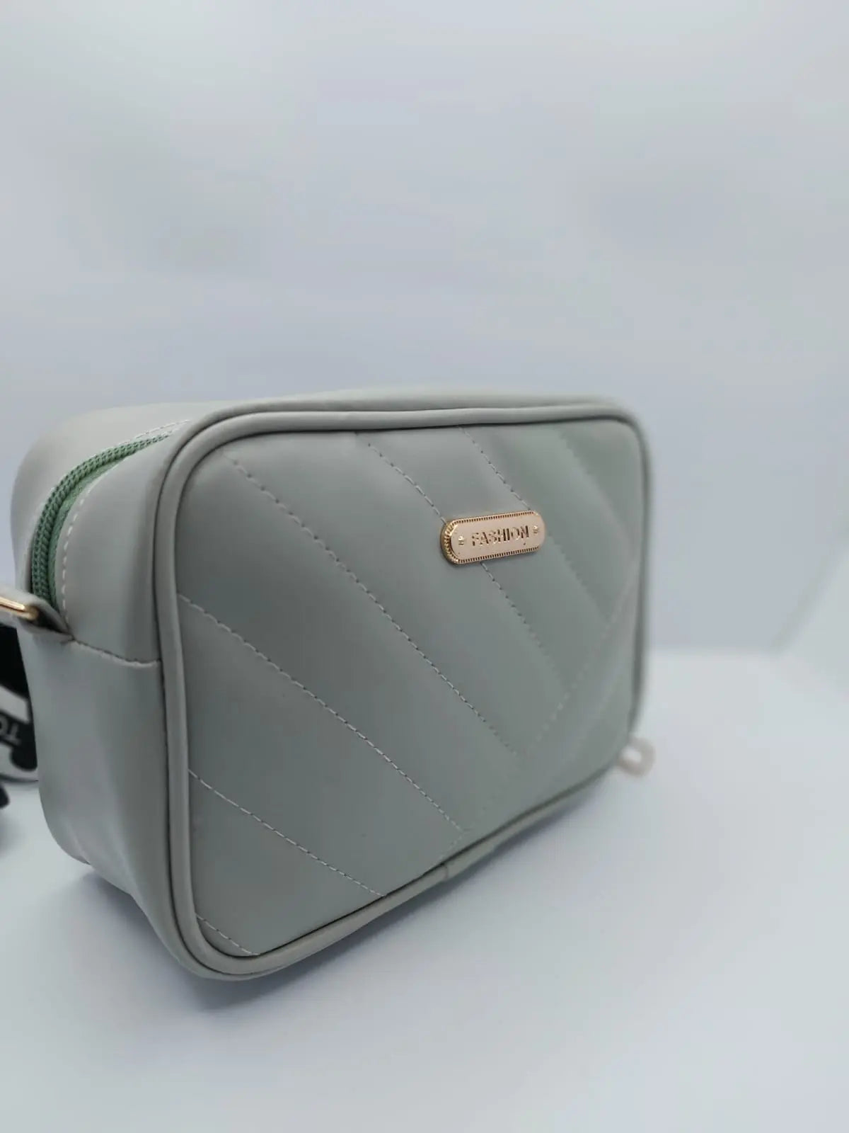 Light Grey Urban Grace Crossbody Bag with quilted design, gold-tone logo, and adjustable black-and-white strap. Stylish and functional for daily use