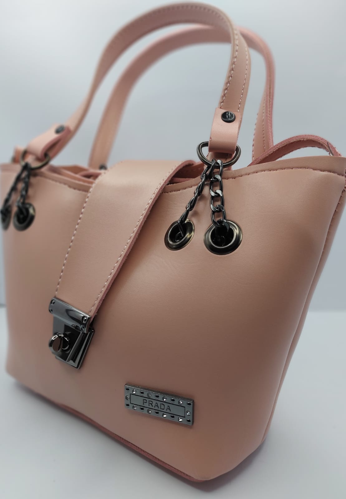 Radiant Peach tote bag with metallic twisted lock, made from premium PU leather. Features hand tote and adjustable shoulder straps, dual zippers for storage, and a sleek solid design with metallic details. Perfect for daily use or special occasions