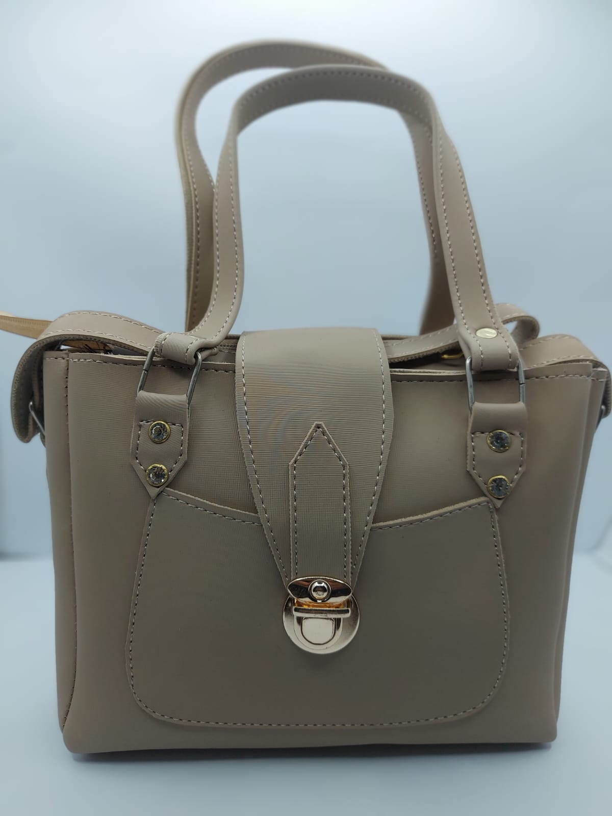 Warm Beige Regal Carry Tote Bag made of premium synthetic leather with neat stitching. Features a gold-tone lock closure, a front pocket for easy access, and an internal zippered compartment for organization. Offers dual carrying options: hand tote and adjustable shoulder strap