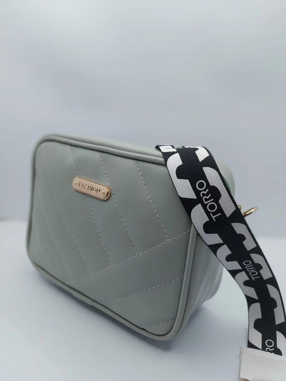 Light Grey Urban Grace Crossbody Bag with quilted design, gold-tone logo, and adjustable black-and-white strap. Stylish and functional for daily use