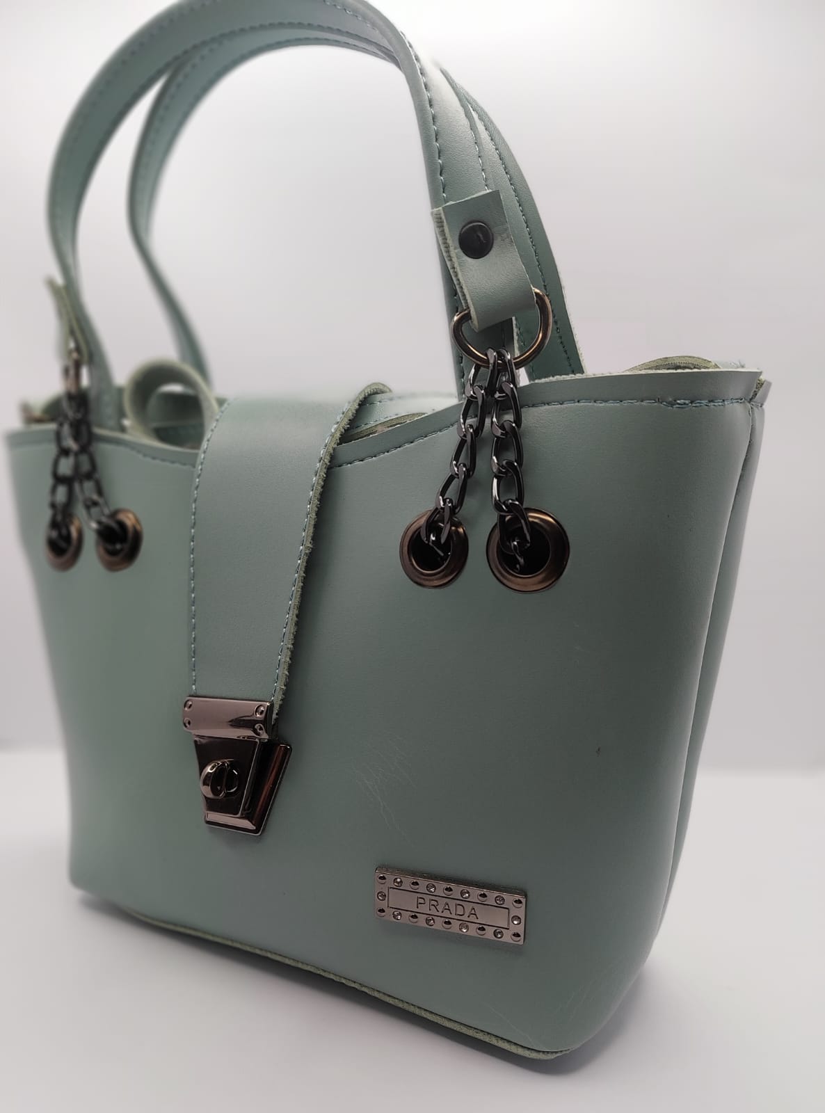 Mint Green tote bag with metallic twisted lock, crafted from premium PU leather. Features hand tote and adjustable shoulder straps, dual zippers fot storage, and a sleek solid design with metallic details. Ideal for daily use or special occasions