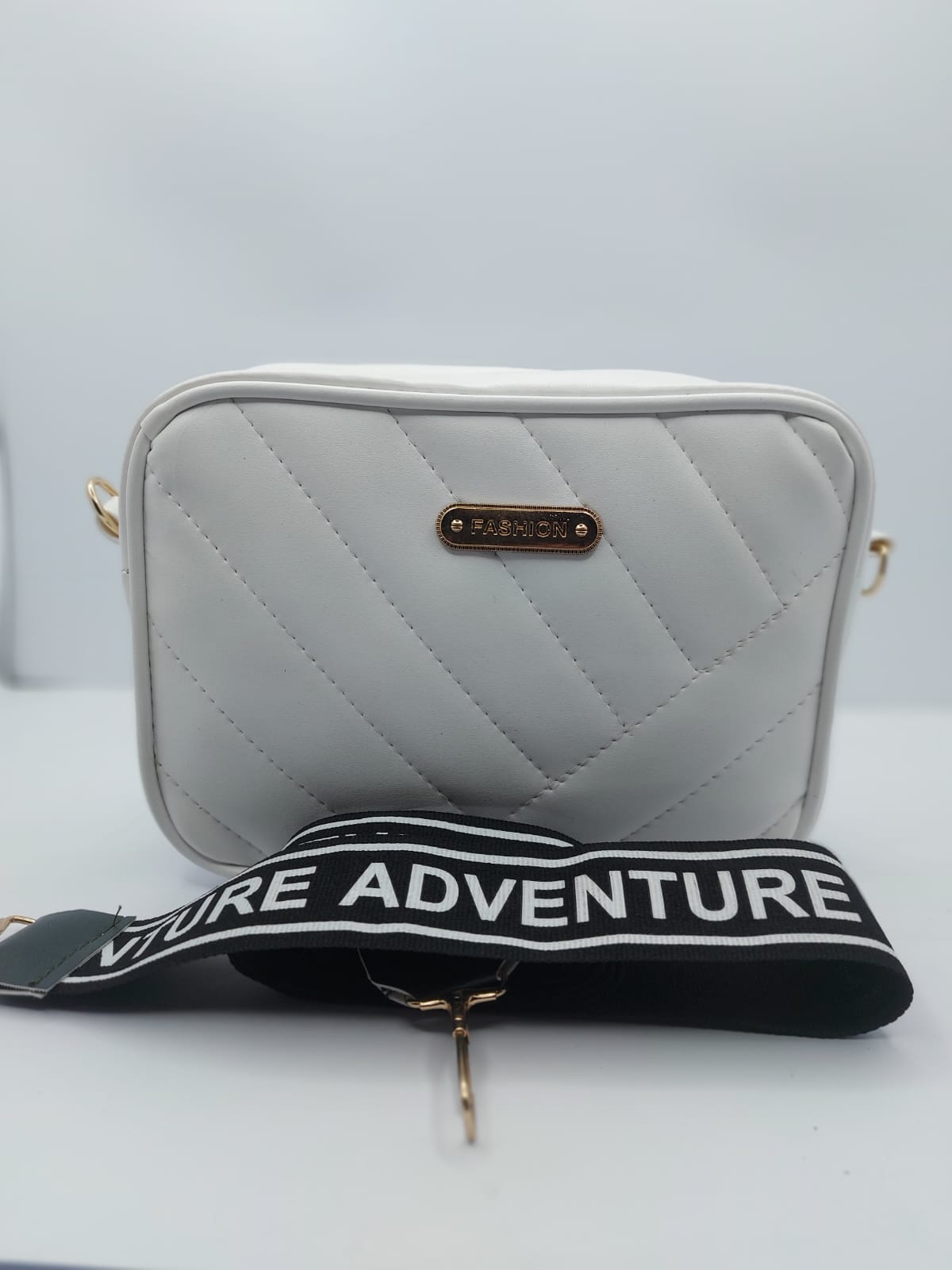 White Urban Grace Crossbody Bag with quilted design, gold-tone logo, and adjustable black-and-white strap. Stylish and functional for daily use